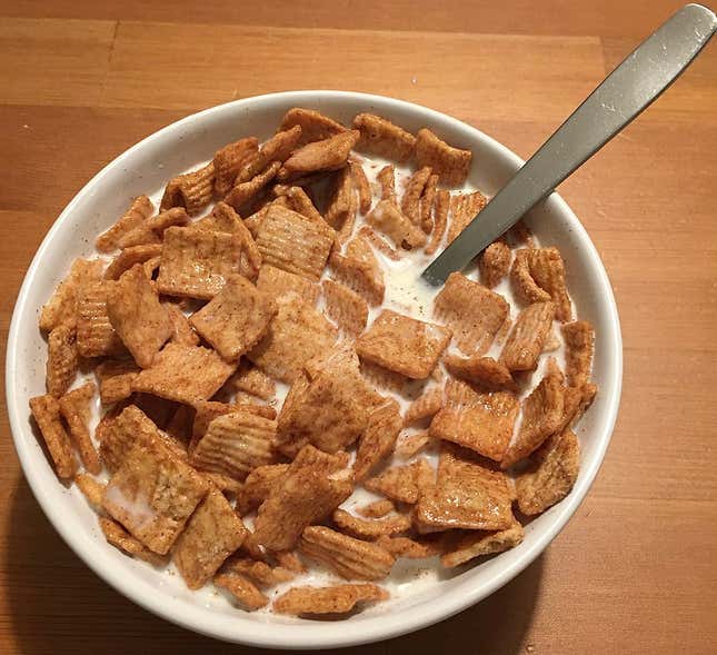 A white bowl full of Cinnamon Toast Crunch cereal and milk sits on a wooden table