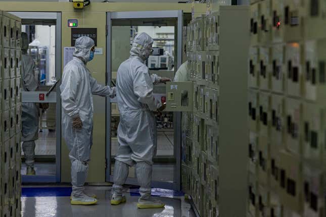 two people wearing white clean room suits seen from a "hallway" made up of what look like lockers