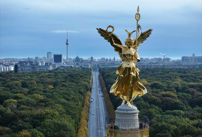 aerial view of the golden statue with the autobahn running under it between trees, the Reichstag, the broadcast tower at Alexanderplatz, Dom cathedral and the Brandenburg Gate are behind it too