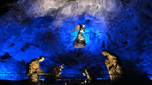 in the side of a salt mine, an angel hovers above four statues below; the whole image is tinged with blue