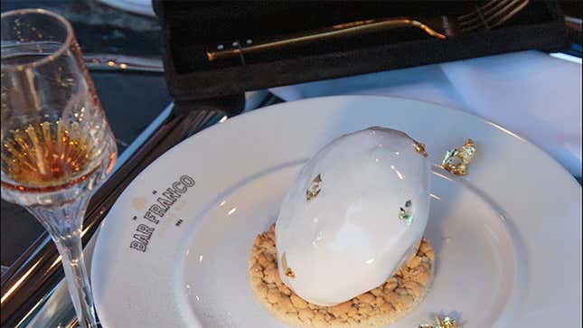 a Bar Franco plate with a cookie with a dollop of cream on it, a crystal goblet with cognac in it, and a gold fork encrusted with diamonds