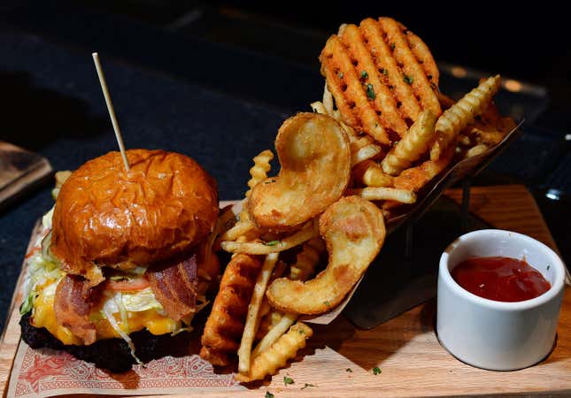 A bacon burger sits to the left of various cuts of french fries and ketchup