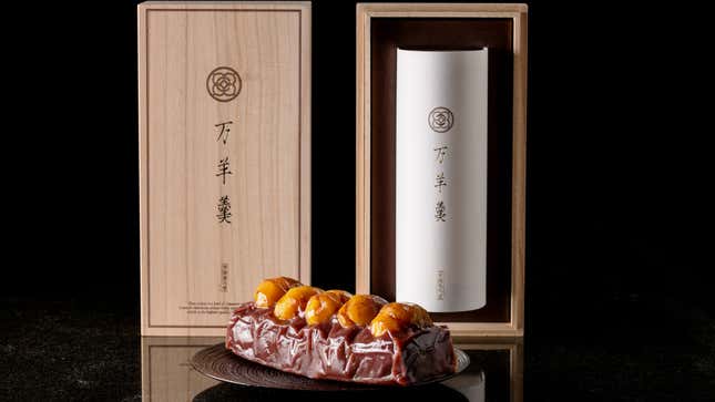 A chestnut-colored log with candied nuts on top in front of a black background and a wooden box