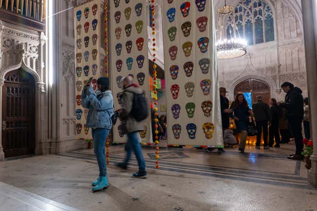 Tourists walk around a church where three banners of colorful skulls hang from the ceiling