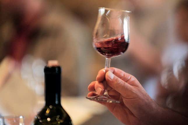 An artistically blurred image of a hand swirling a glass of red wine with a bottle in the background