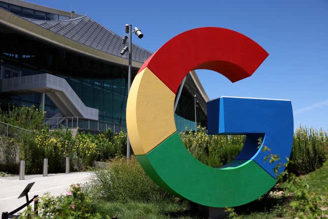 A giant, multicolored Google logo outside a building among flowers and grass