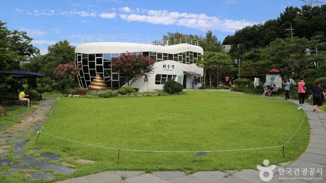 A white, toilet-shaped building with lots of glass windows sits back behind a green lawn